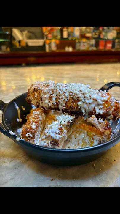 A cast-iron dish filled with roasted corn topped with creamy dressing and a sprinkle of cheese.