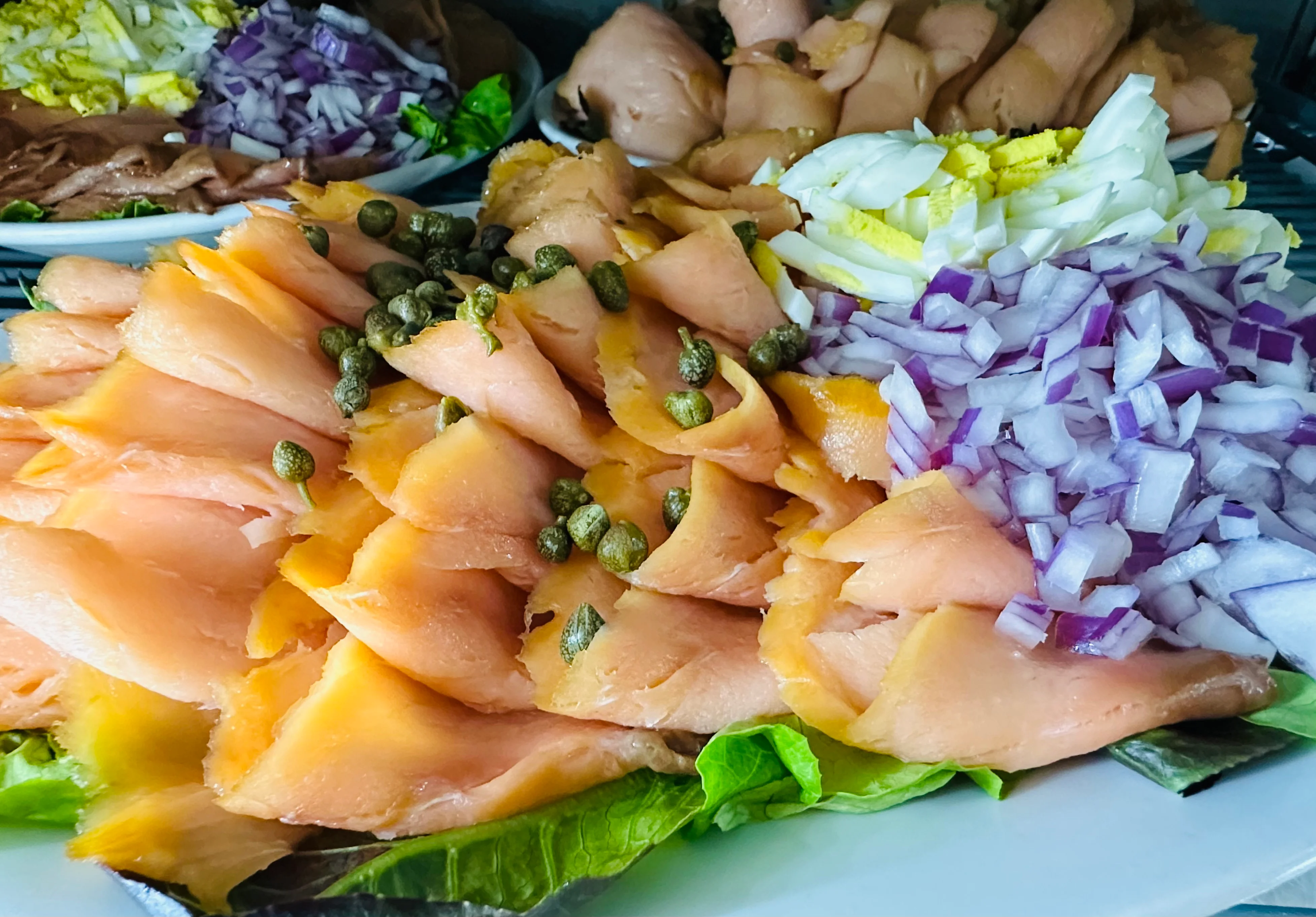 A platter featuring layers of smoked salmon with capers, accompanied by diced onions and lettuce.