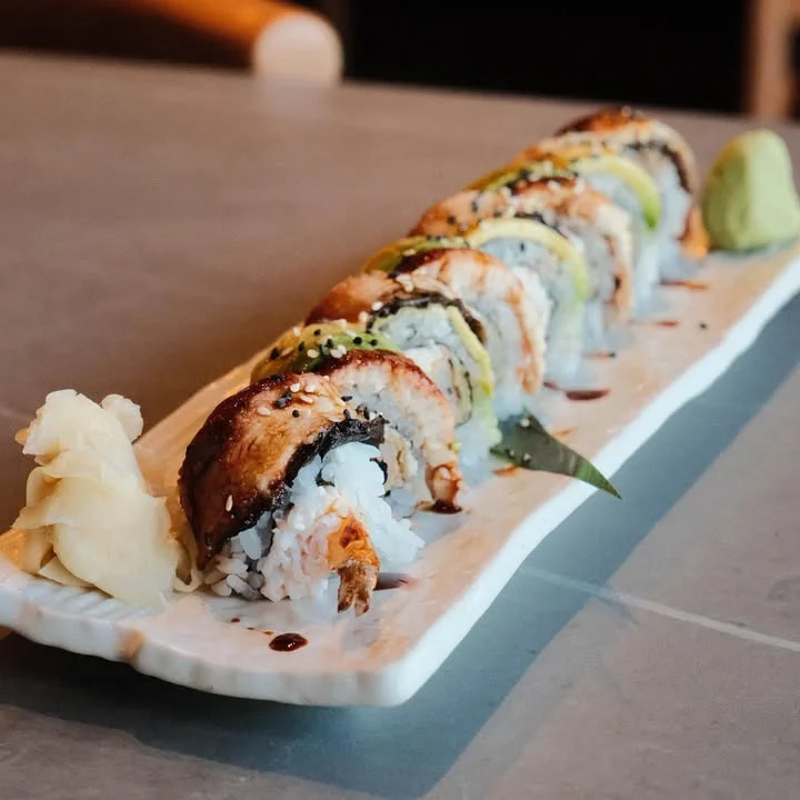A selection of sushi rolls arranged on a white plate, garnished with wasabi and pickled ginger, showcasing colorful layers of ingredients.