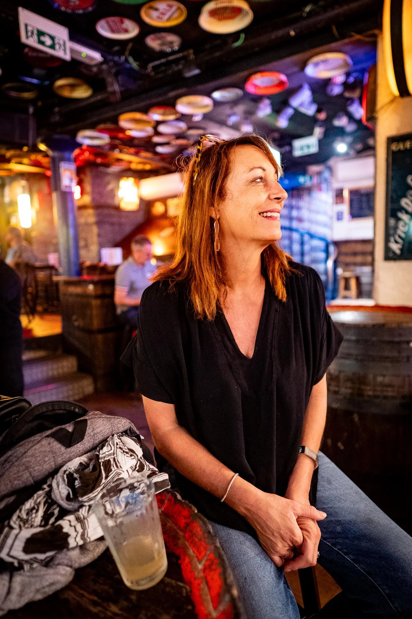 Woman smiling in a lively bar with colorful decor and warm lighting.