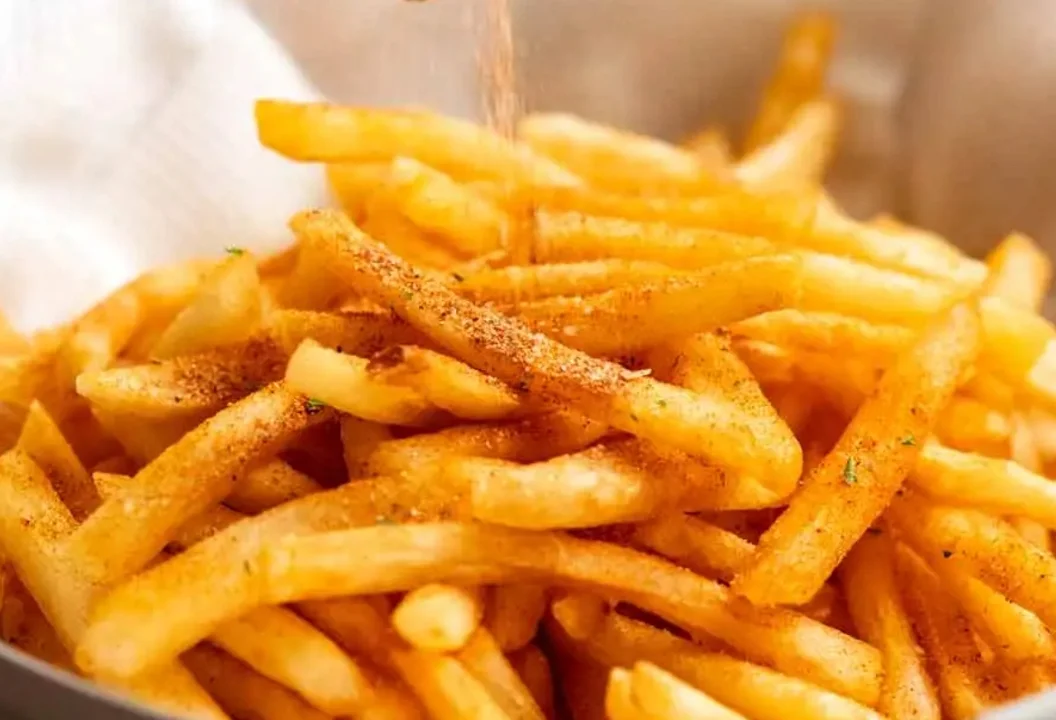 A serving of golden crispy French fries sprinkled with seasoning, presented in a bowl.