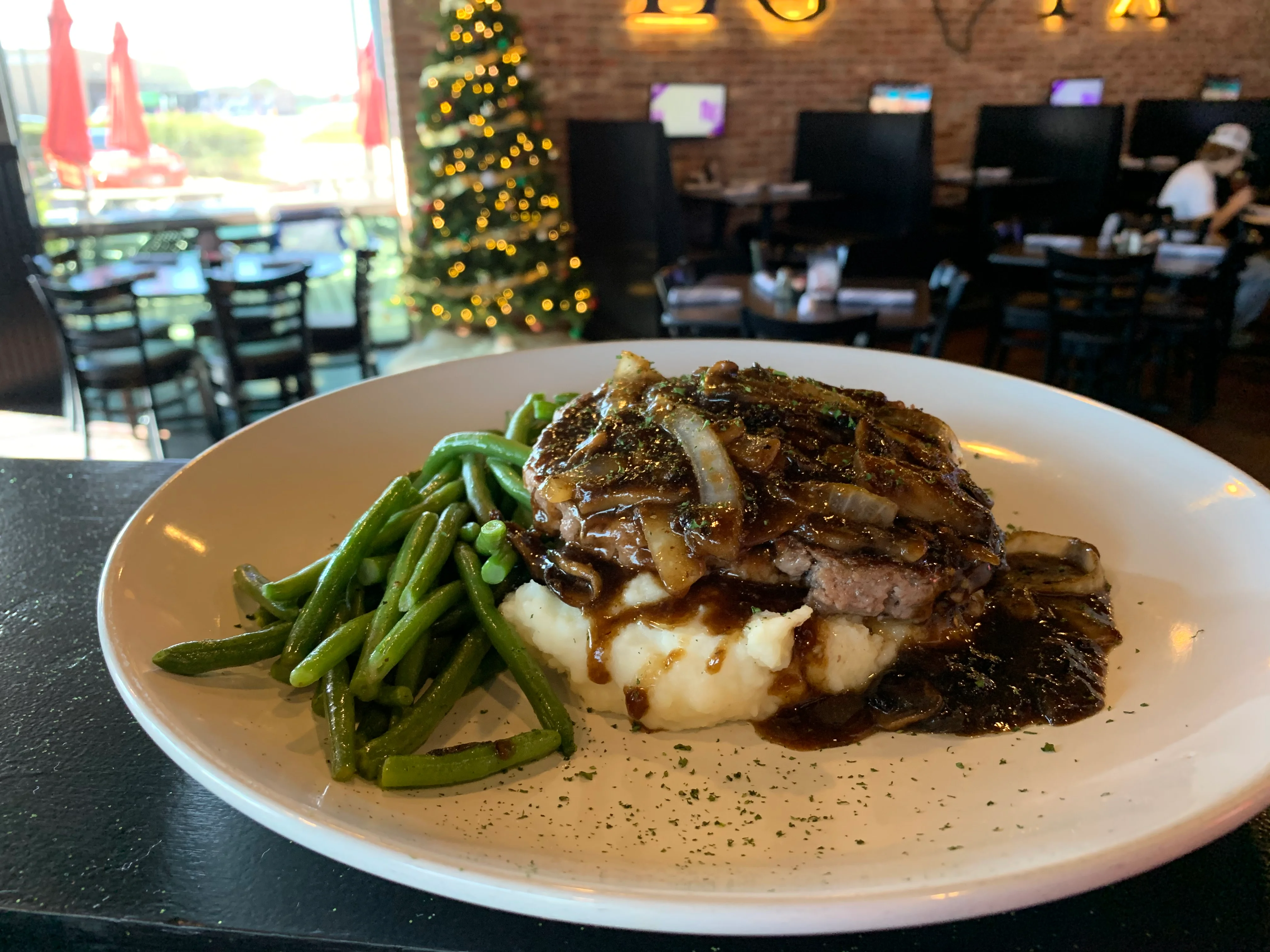 A plate of savory meatloaf topped with onions and gravy, served with mashed potatoes and green beans.