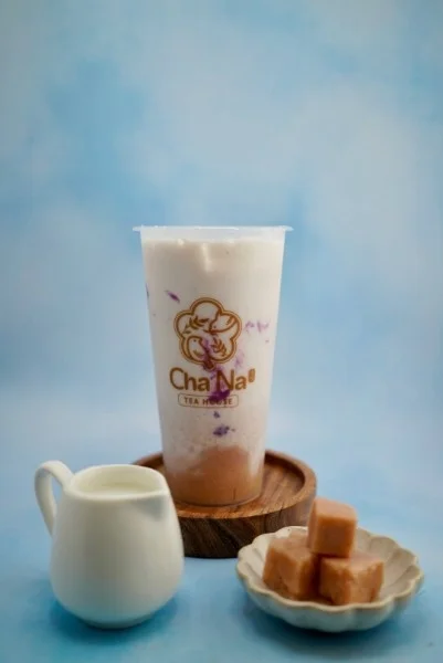 A refreshing drink featuring a creamy layer on top, served in a branded cup with a side of sweet treats and milk.