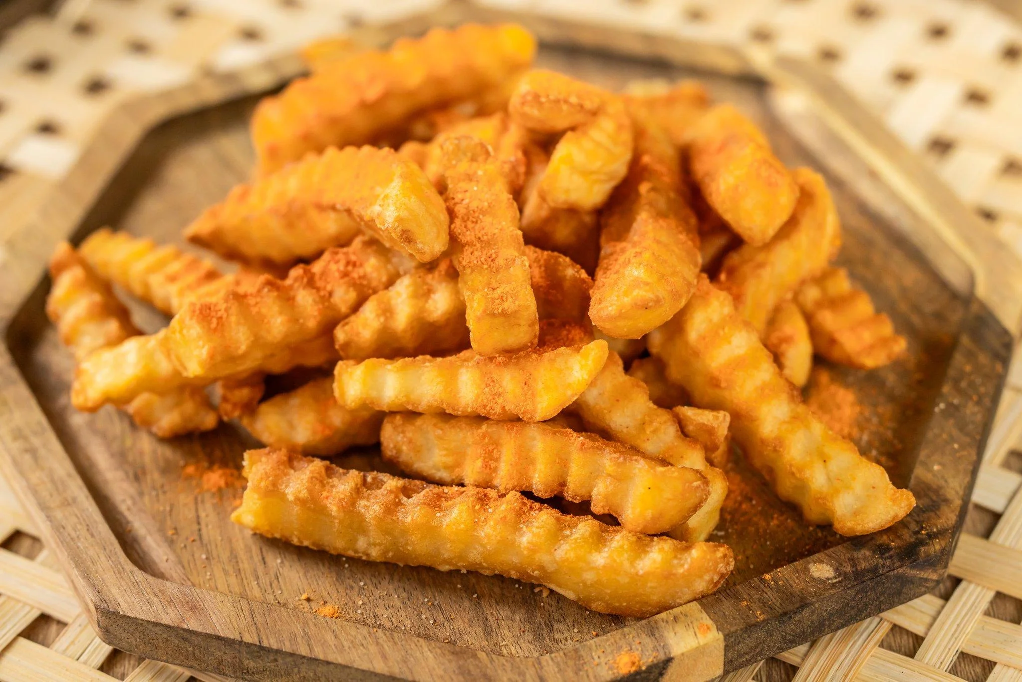 Crispy crinkle-cut fries stacked on a wooden plate, showcasing their golden color and texture.