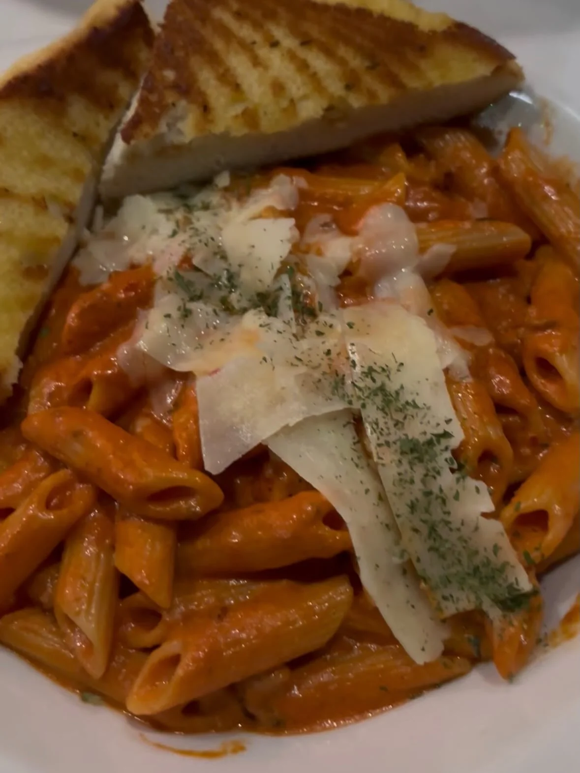 A plate of penne pasta in a creamy tomato sauce, garnished with cheese and herbs, accompanied by slices of toasted bread.