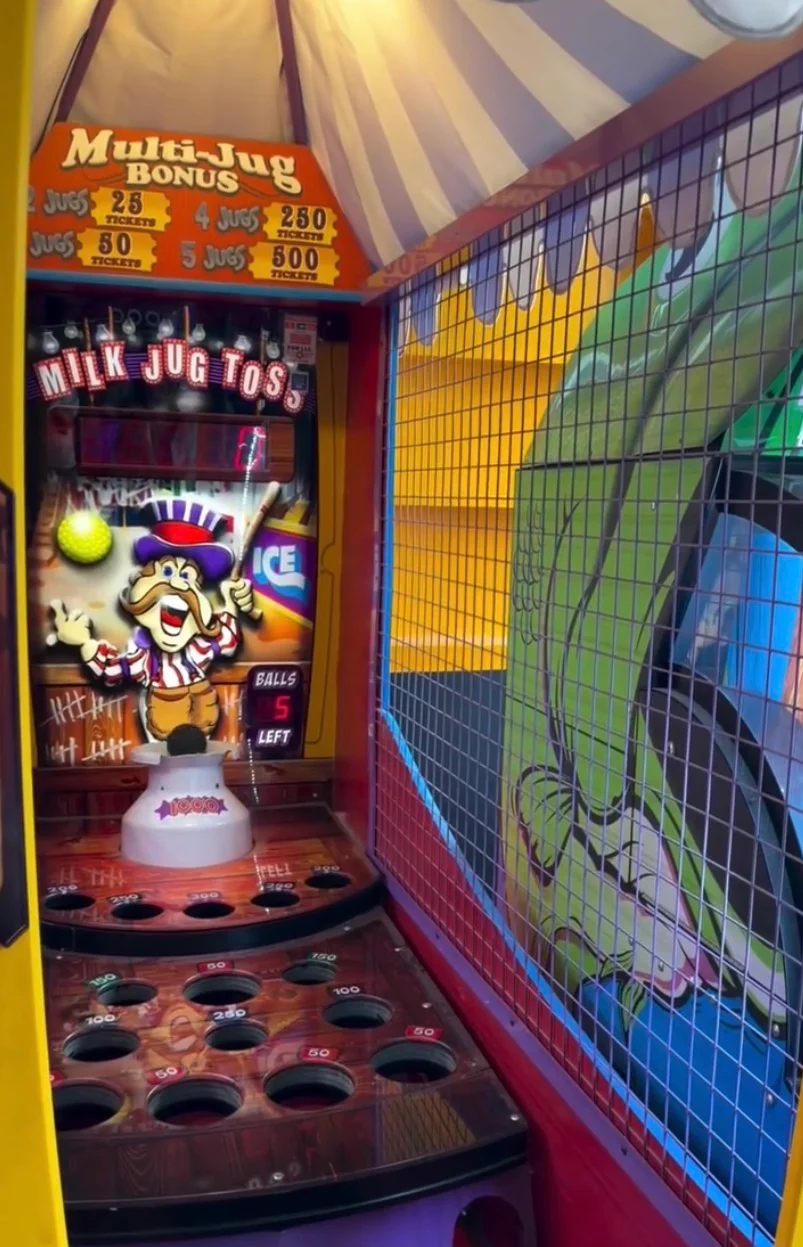 Colorful carnival milk jug toss game booth with ball targets and striped canopy