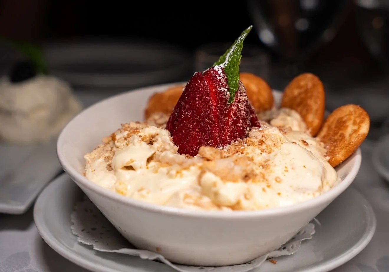A bowl of dessert featuring creamy filling, topped with a strawberry and garnish, accompanied by cookies.