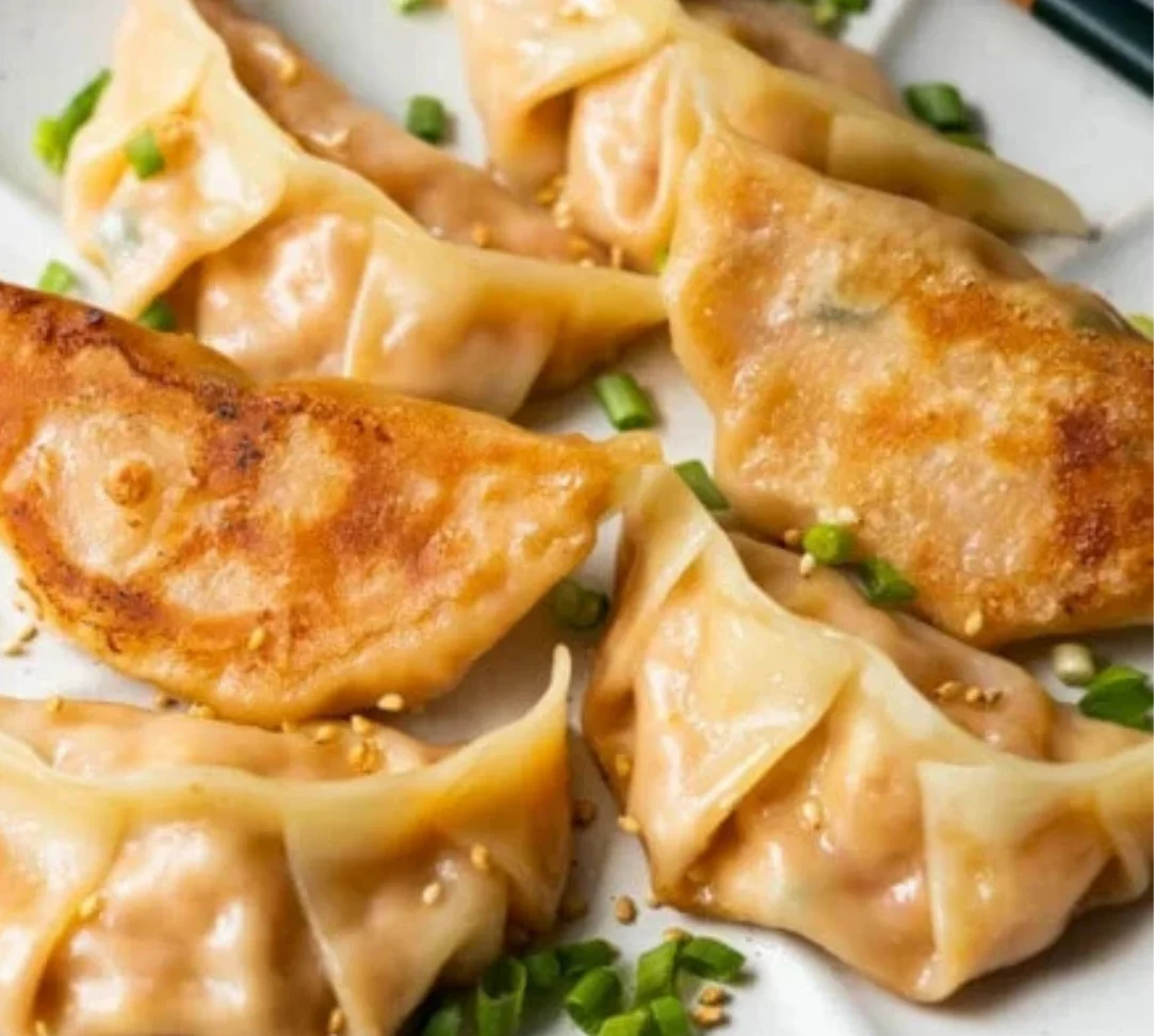 Delicious dumplings with a golden brown sear and green onions on a plate.