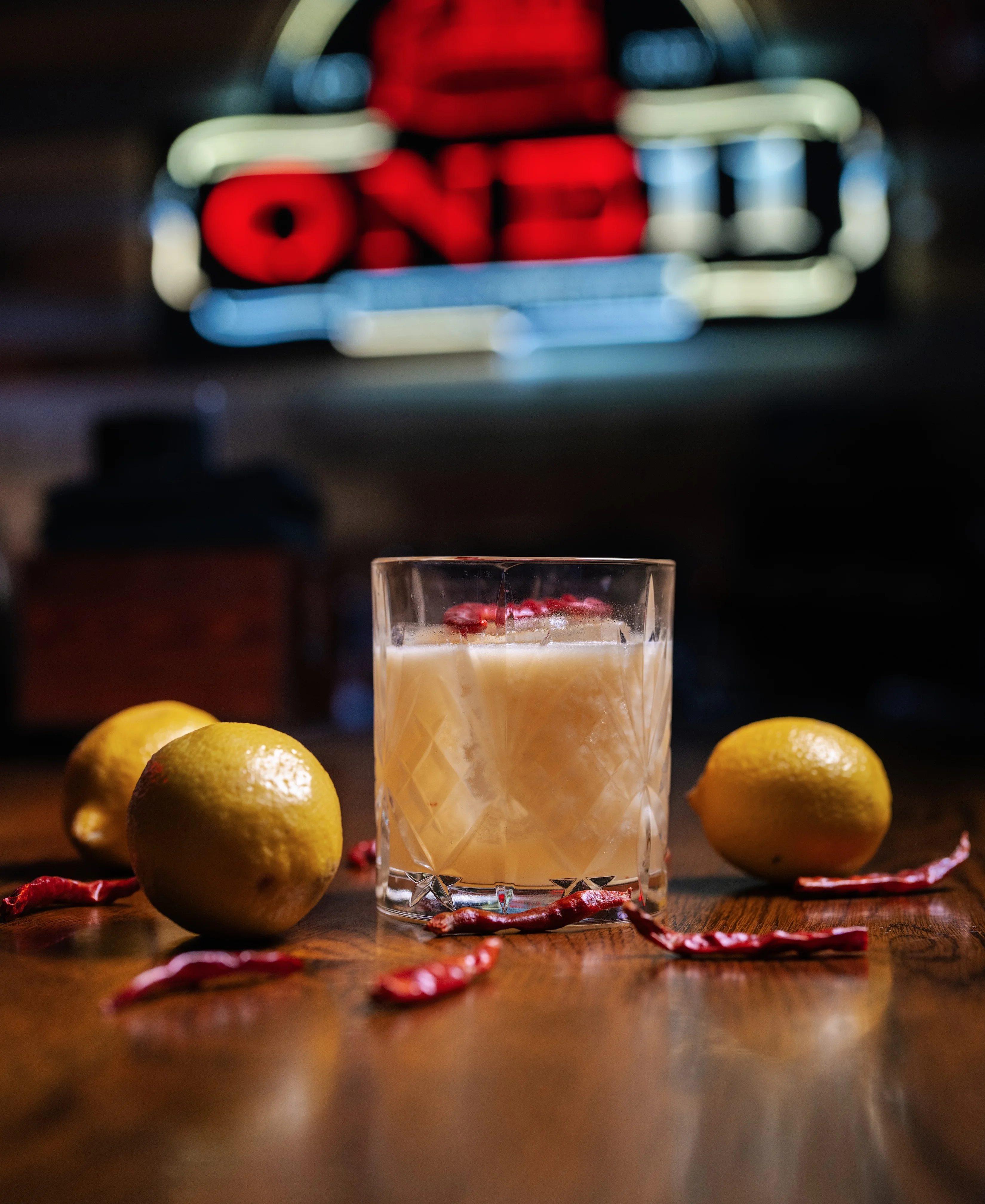 Craft cocktail with lemon and chili garnish on a wooden bar