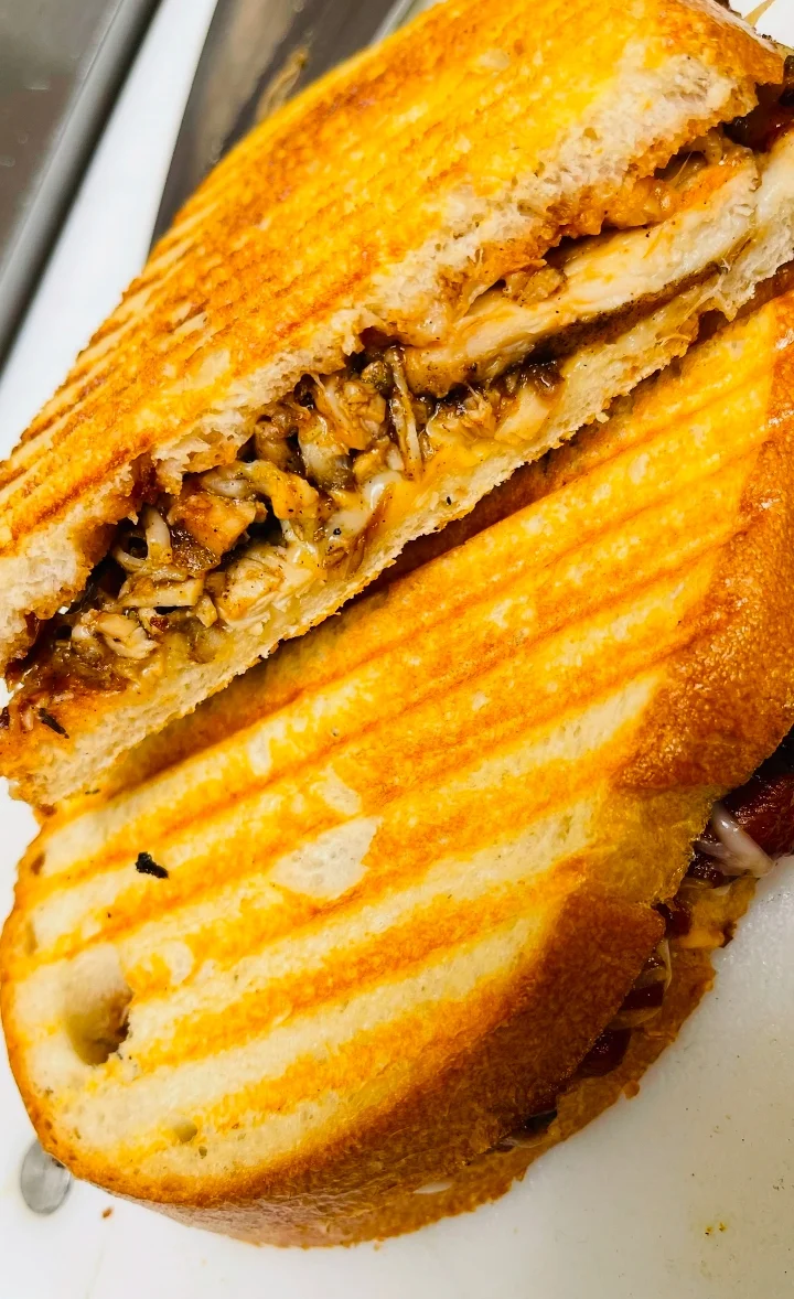 A grilled sandwich filled with shredded chicken, sliced open to show its contents, showcasing a golden brown exterior.
