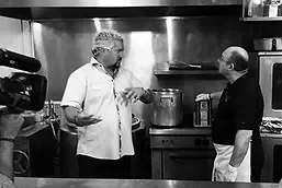 Two chefs discussing cooking techniques in a restaurant kitchen