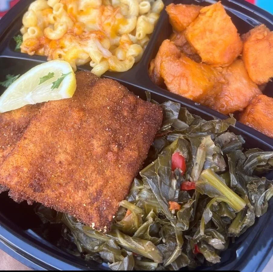 A meal divided into sections featuring fried fish, collard greens, macaroni and cheese, and sweet potatoes.