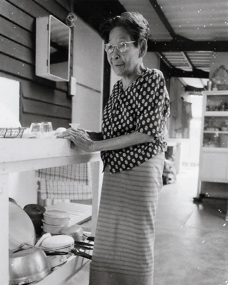 Elderly woman in traditional attire at a rustic kitchen counter