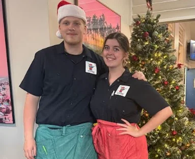 Two restaurant staff members in festive attire by a Christmas tree