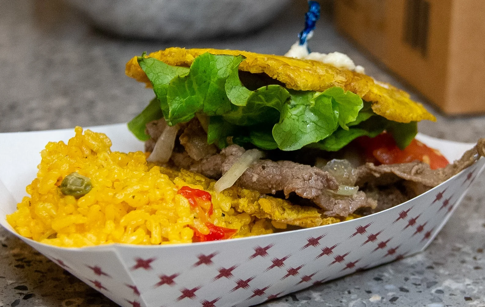 A serving of beef and vegetable-filled tostones with a side of yellow rice. The meal includes fresh lettuce and tomatoes layered between crispy plantain slices.