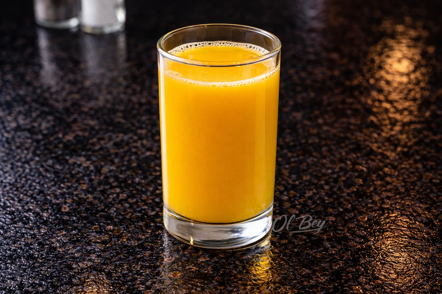 A glass containing a bright orange drink, set on a shiny dark surface.
