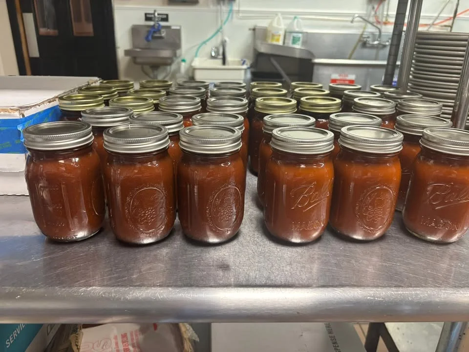 Several jars filled with a reddish-brown sauce lined up on a stainless steel surface.