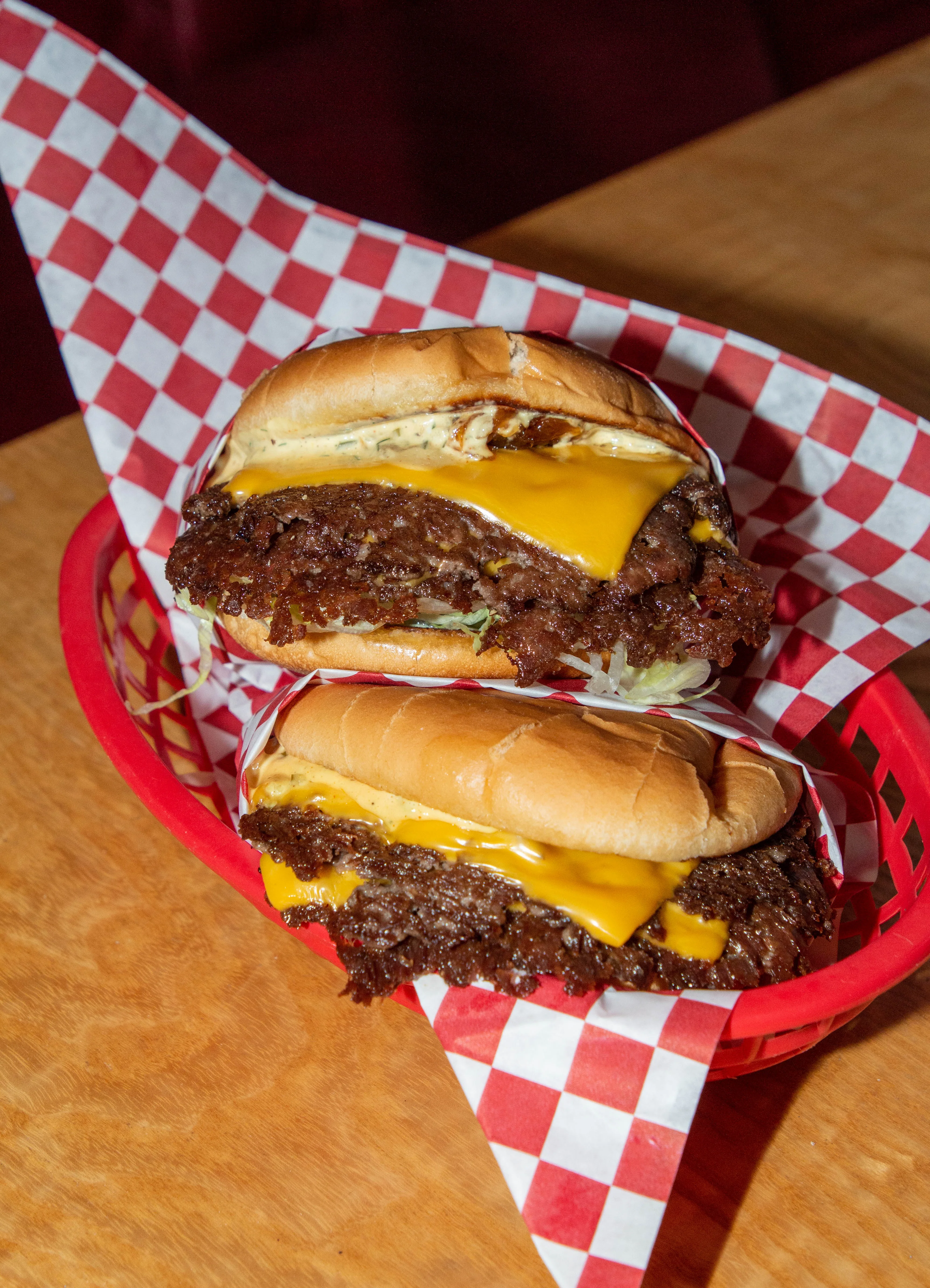 Two cheeseburgers with melted cheese in a red basket with checkered paper.