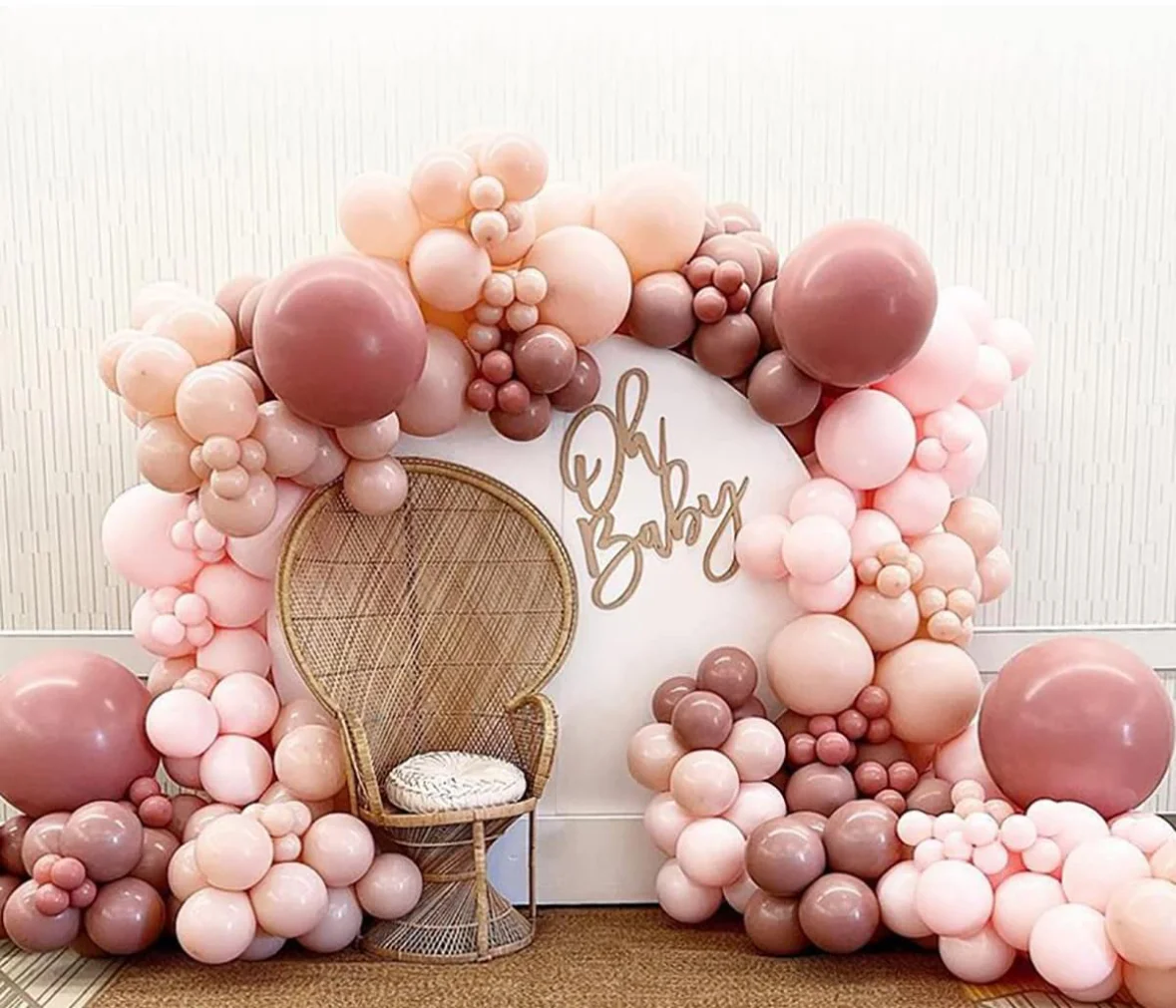 A decorative backdrop featuring a variety of pastel balloons in shades of pink and brown, with a stylish chair and the words 'Oh Baby' elegantly displayed.