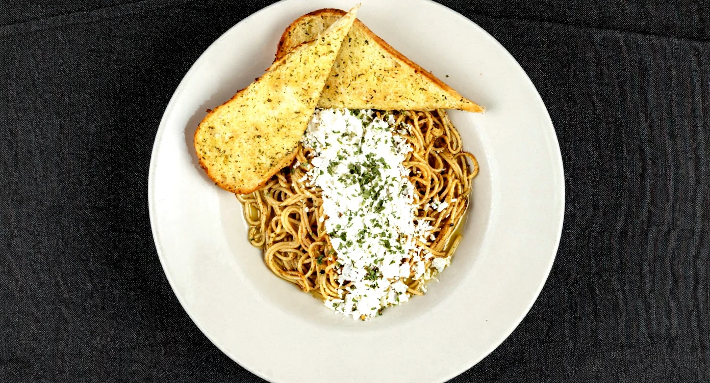 Plate of spaghetti topped with Mizithra cheese and garnished.