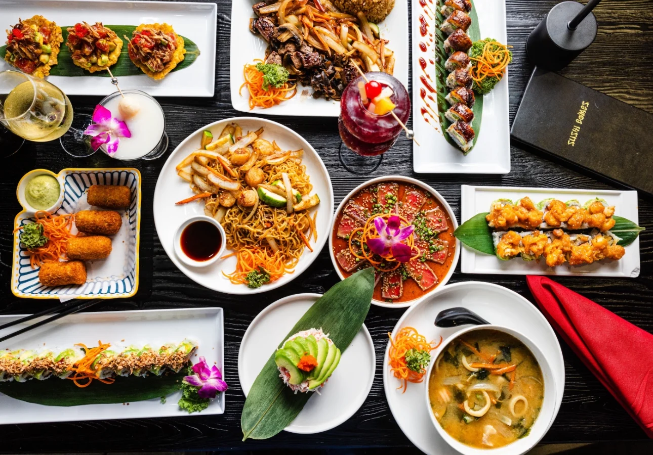 Assorted Asian dishes including sushi and pad thai on a black table