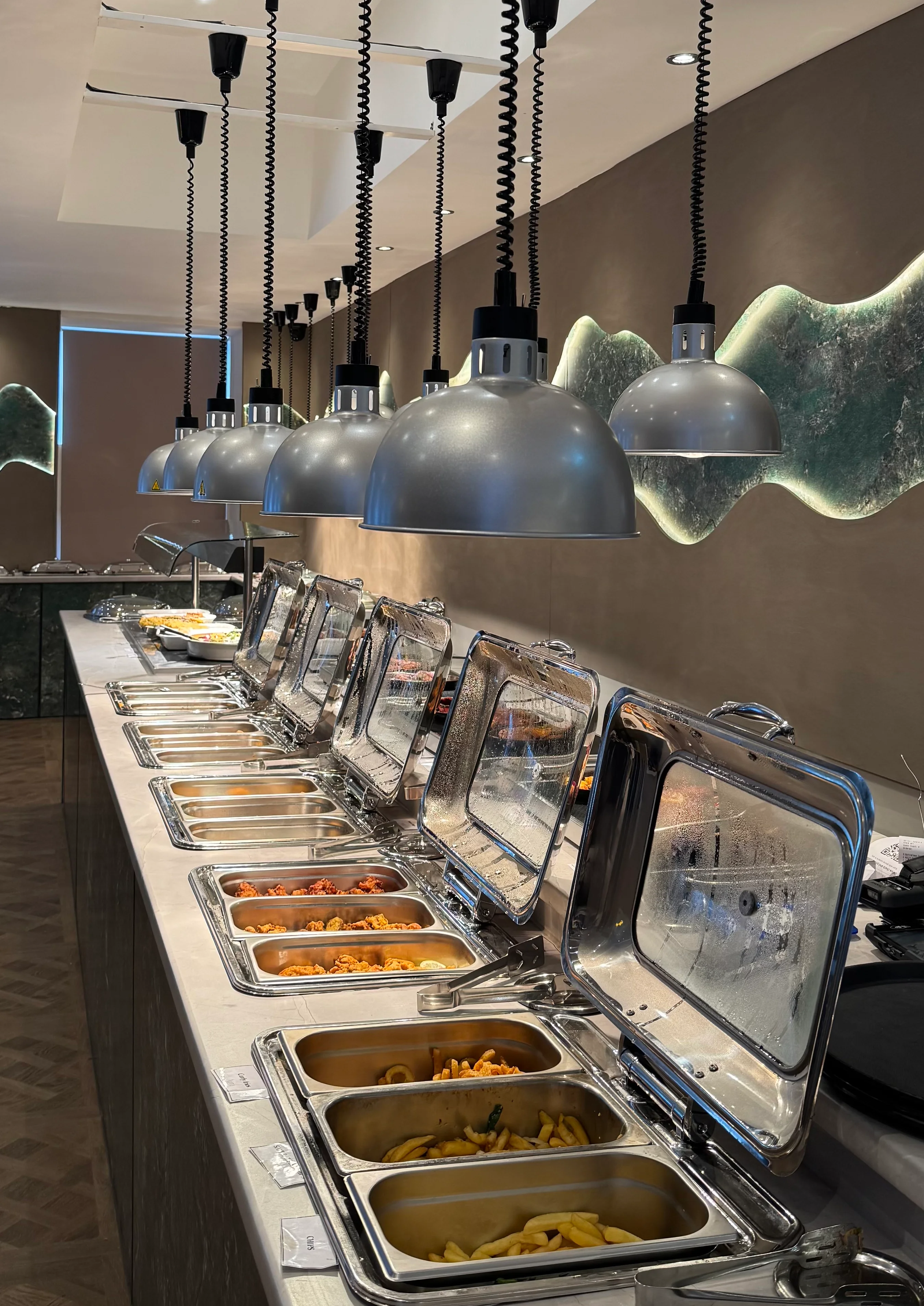 Buffet setup with various food trays and modern lighting in a restaurant.