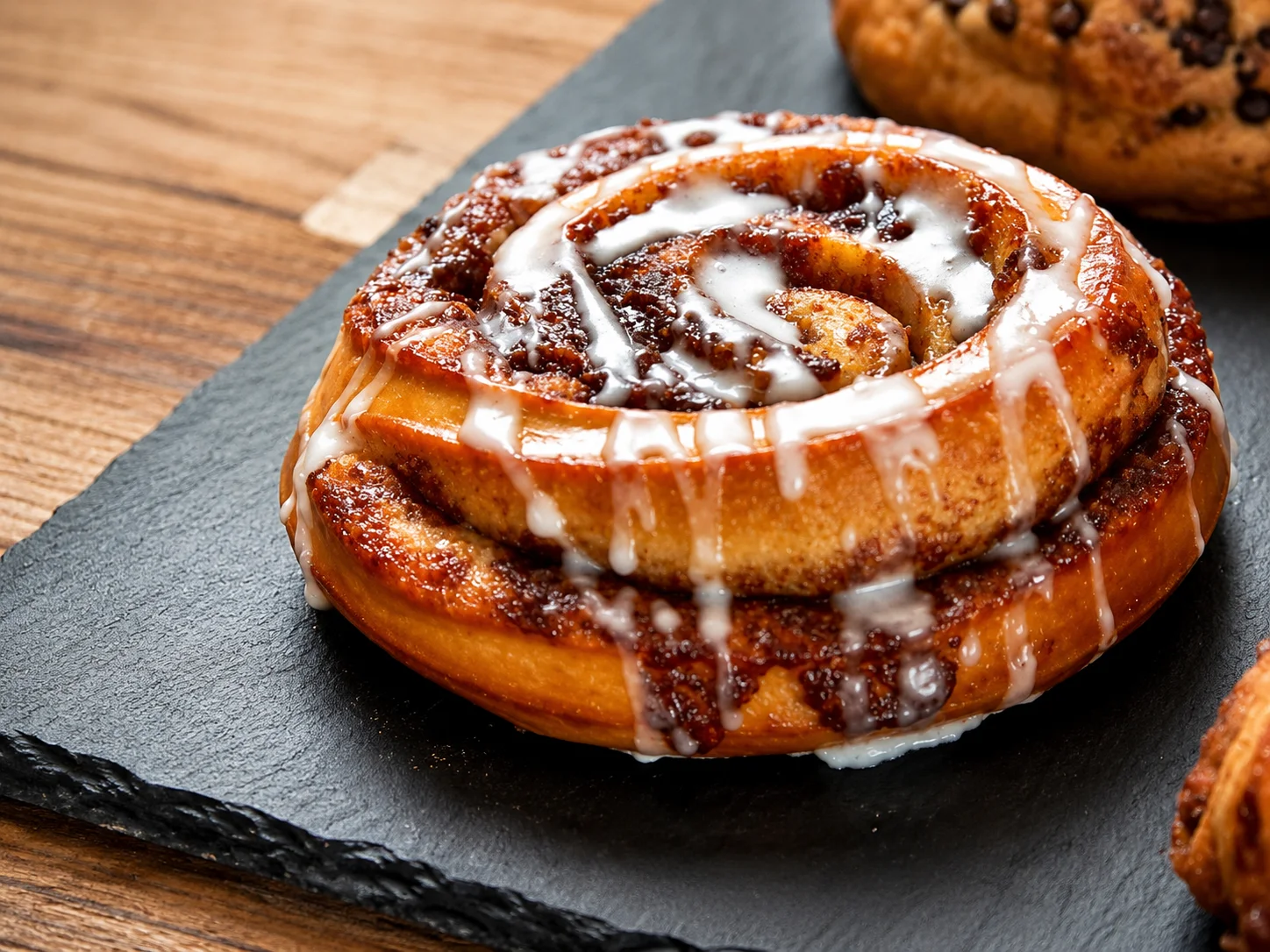 Assorted pastries including cinnamon rolls and almond pastries on a slate board.