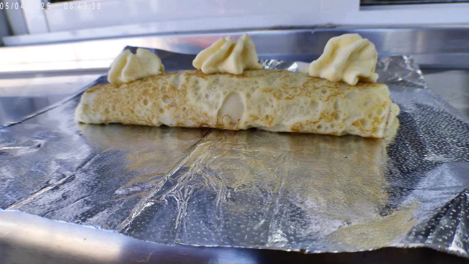 Delicious French crêpe topped with whipped cream on foil