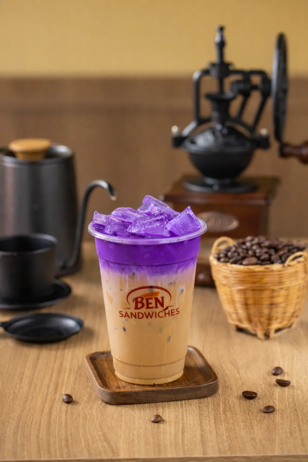 A refreshing iced drink with a purple top layer and a creamy bottom layer, served in a cup. Ice cubes fill the drink, and coffee beans are visible in the background.