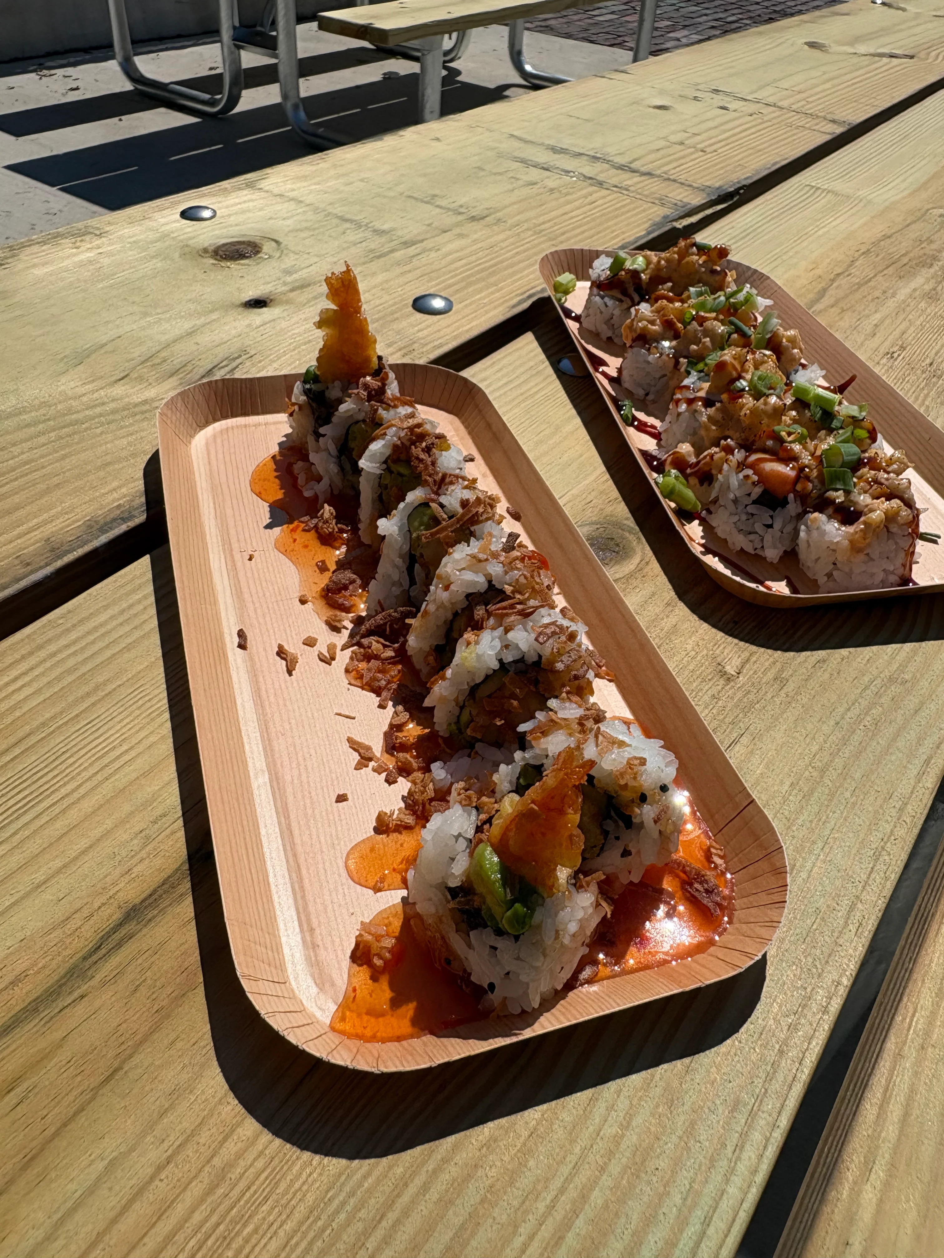 Two sushi platters with various rolls on a wooden table.