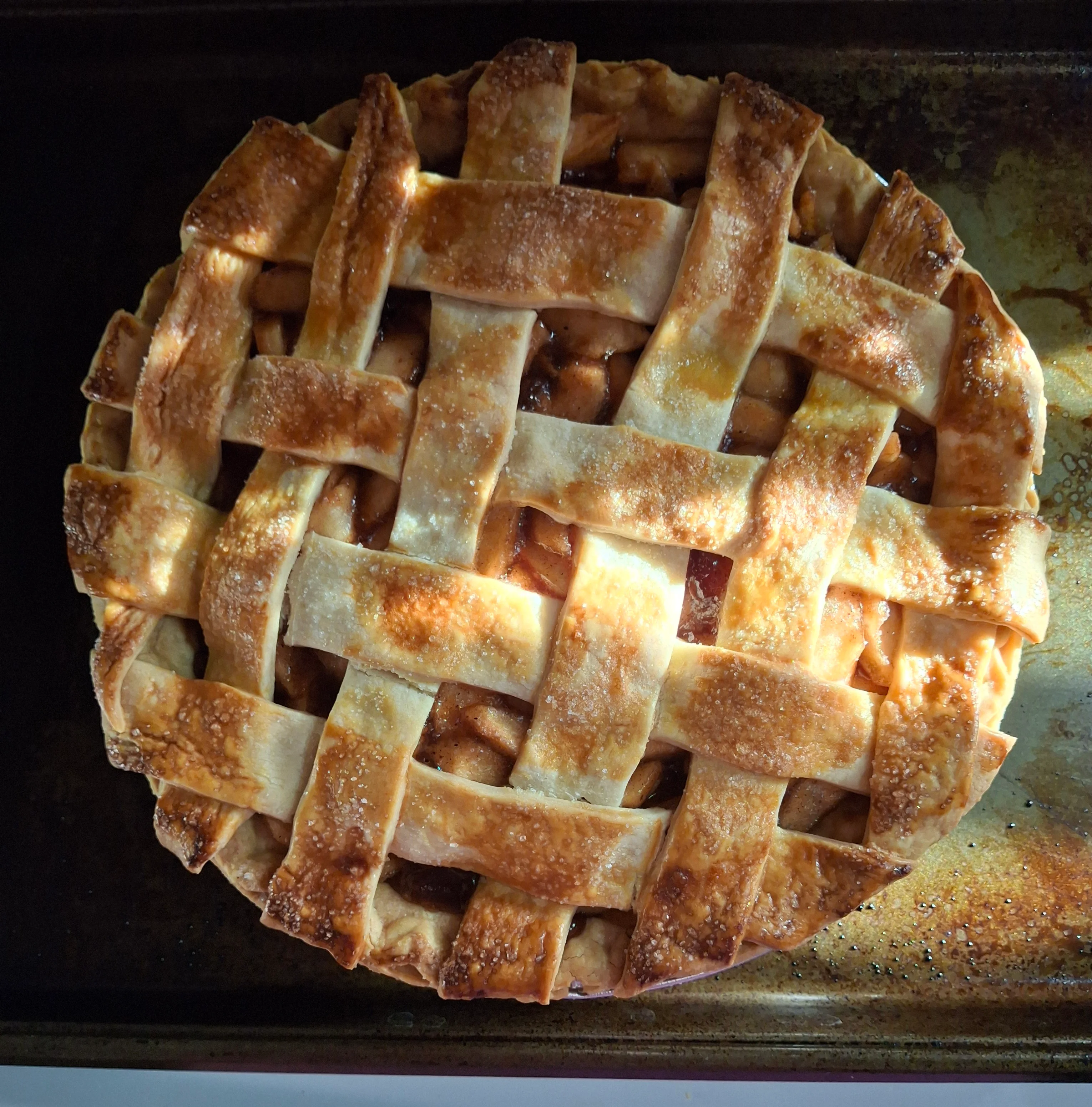 A freshly baked apple pie with a golden, lattice crust, sitting on a baking tray.