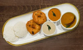 A traditional South Indian meal featuring idli, vada, and three types of chutneys placed on a white platter.