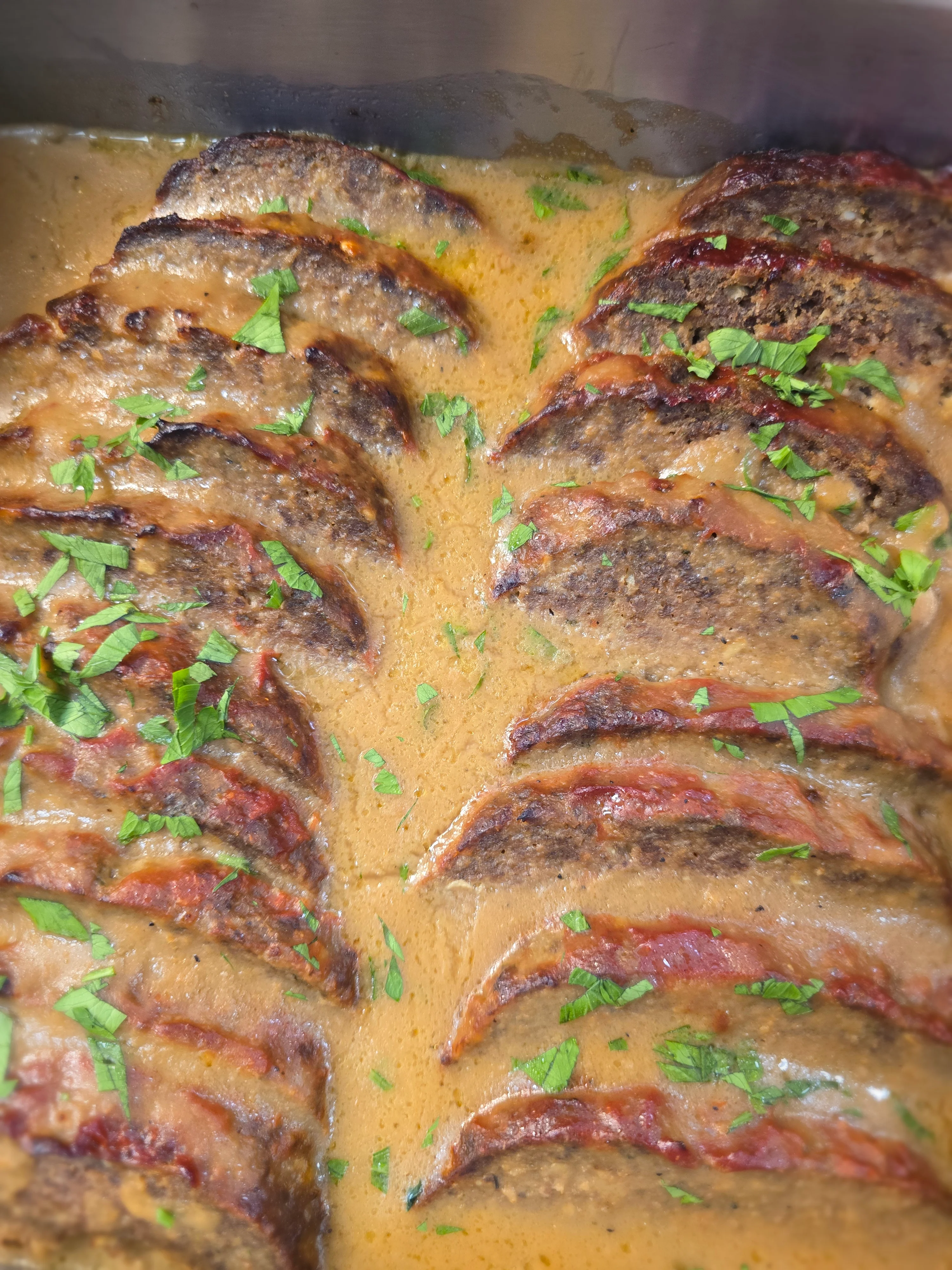 Sliced meatloaf in creamy sauce garnished with fresh herbs