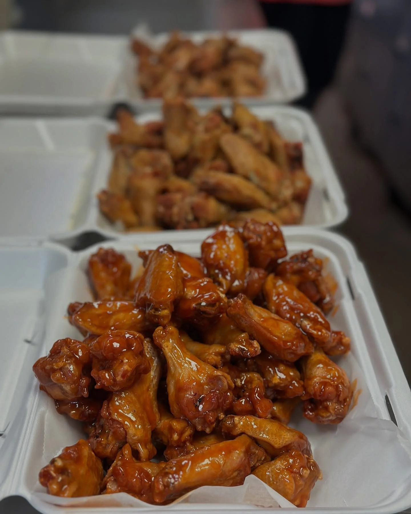 Plates of glazed chicken wings in takeout containers.
