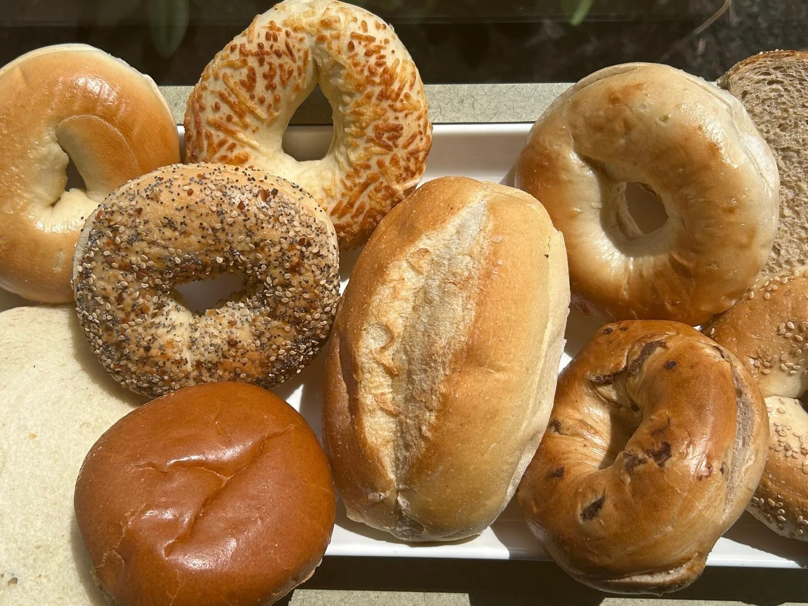 An assortment of bagels and rolls on a white platter, featuring different flavors and textures.