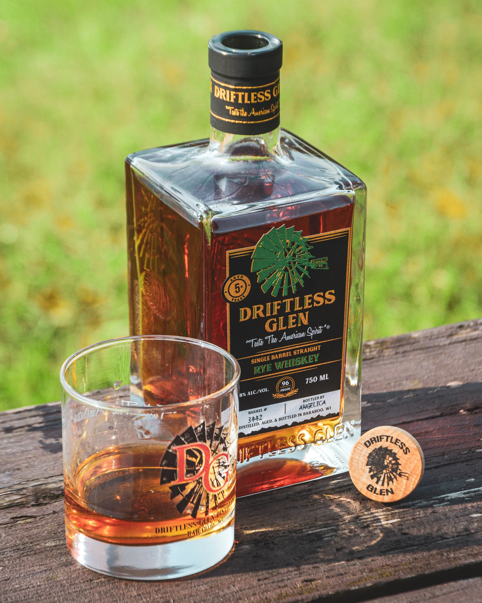 A glass filled with whiskey sits next to a bottle of Single Barrel Rye with the cork next to it
