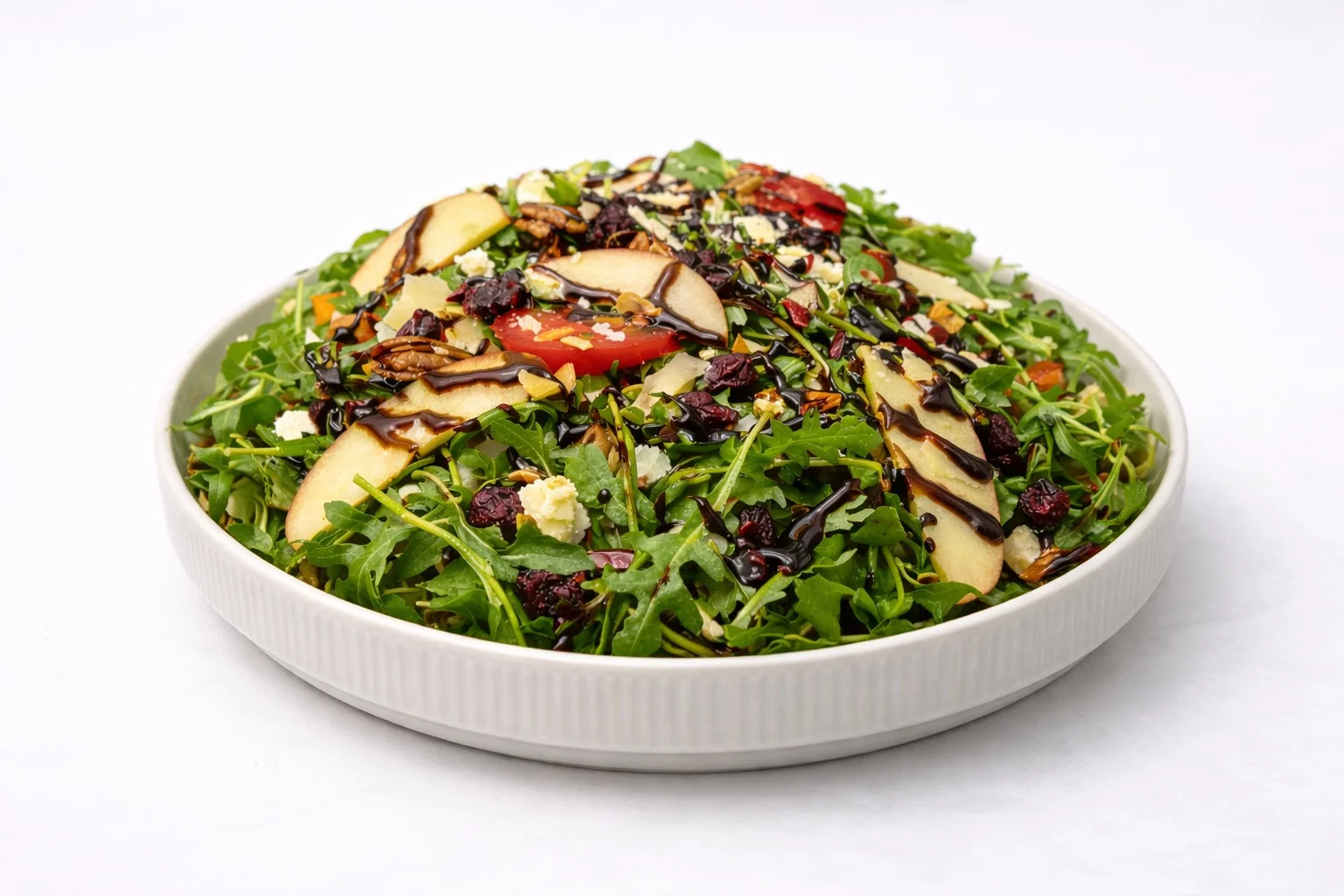 A vibrant salad featuring arugula, sliced apples, and dried fruits, drizzled with a balsamic dressing.