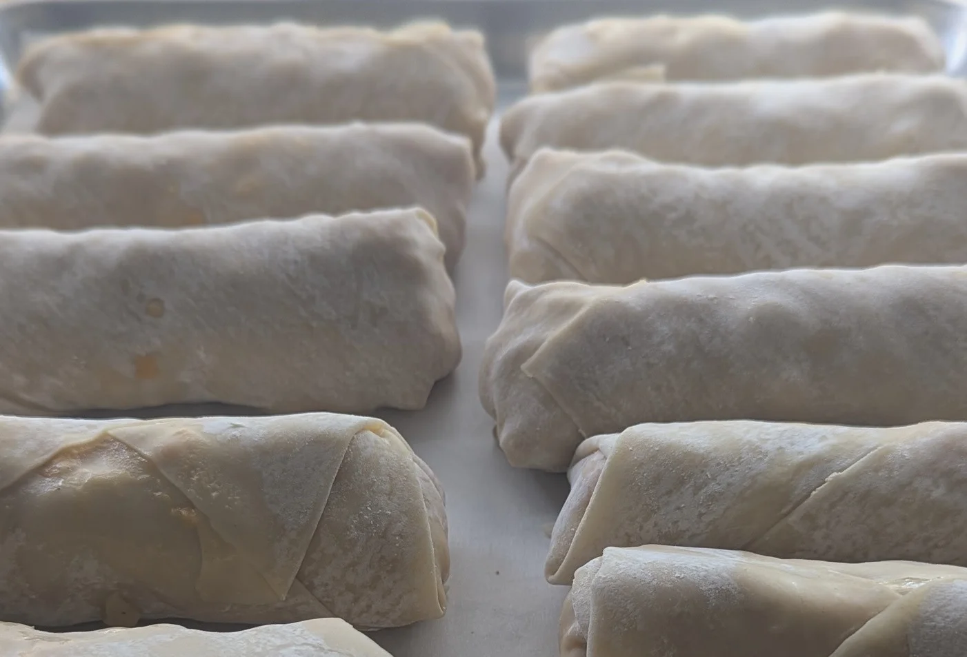 A tray of rolled snacks, likely filled, arranged neatly in a row. The outer layer appears to be a dough or wrapper.