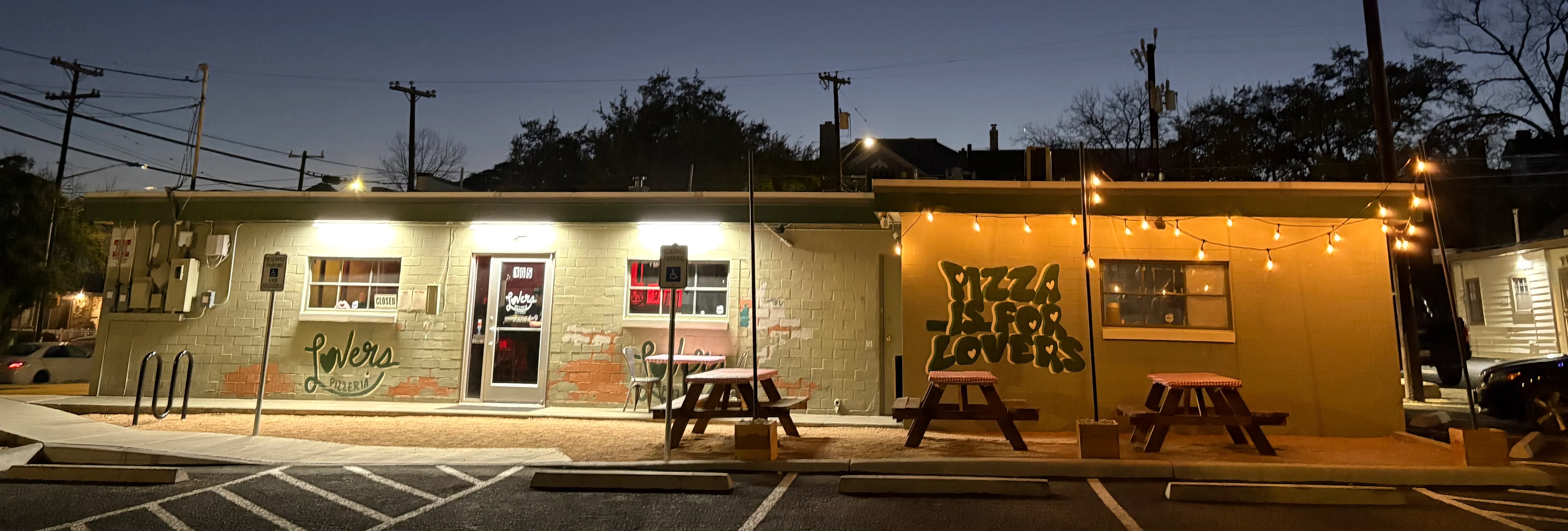 Exterior of a pizzeria at dusk with string lights and a crescent moon.