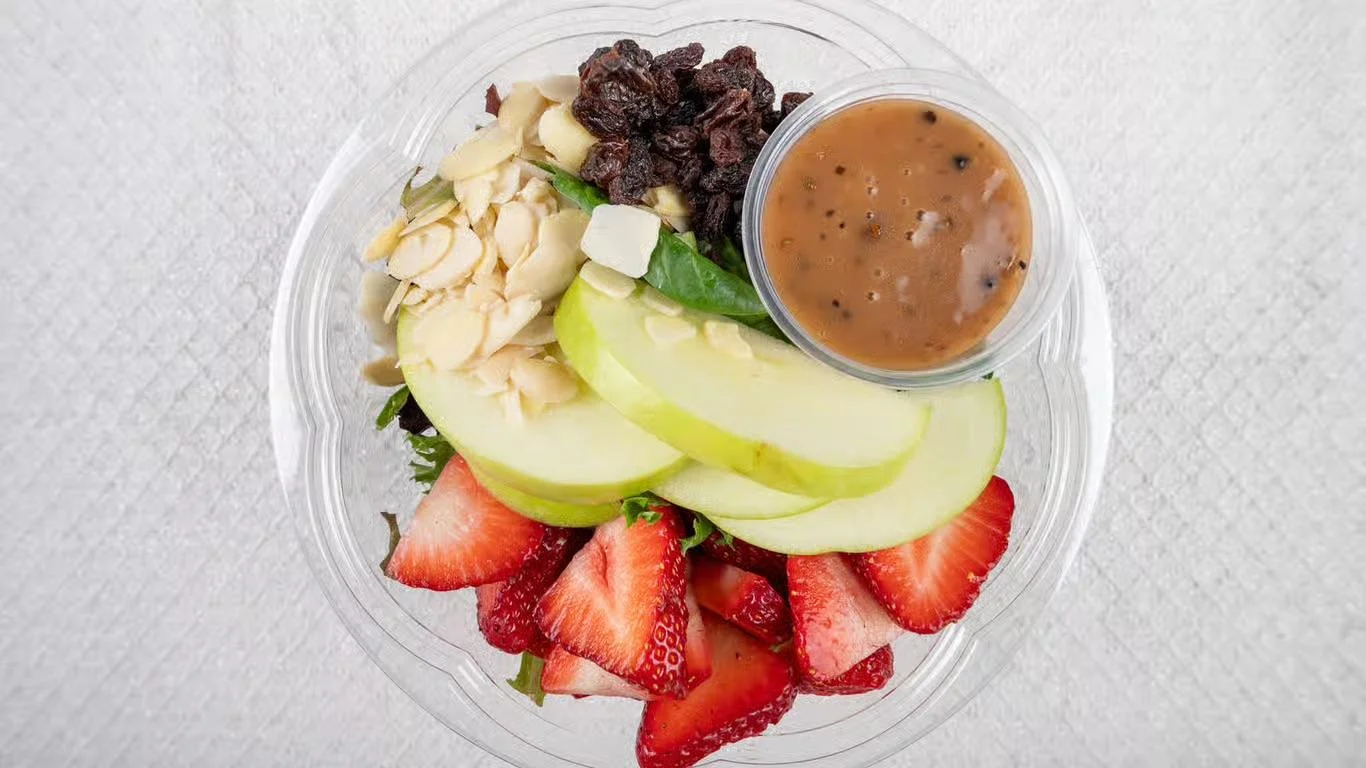 A hand holding a fruit bowl topped with chocolate drizzle, shredded coconut, and an assortment of berries and bananas.