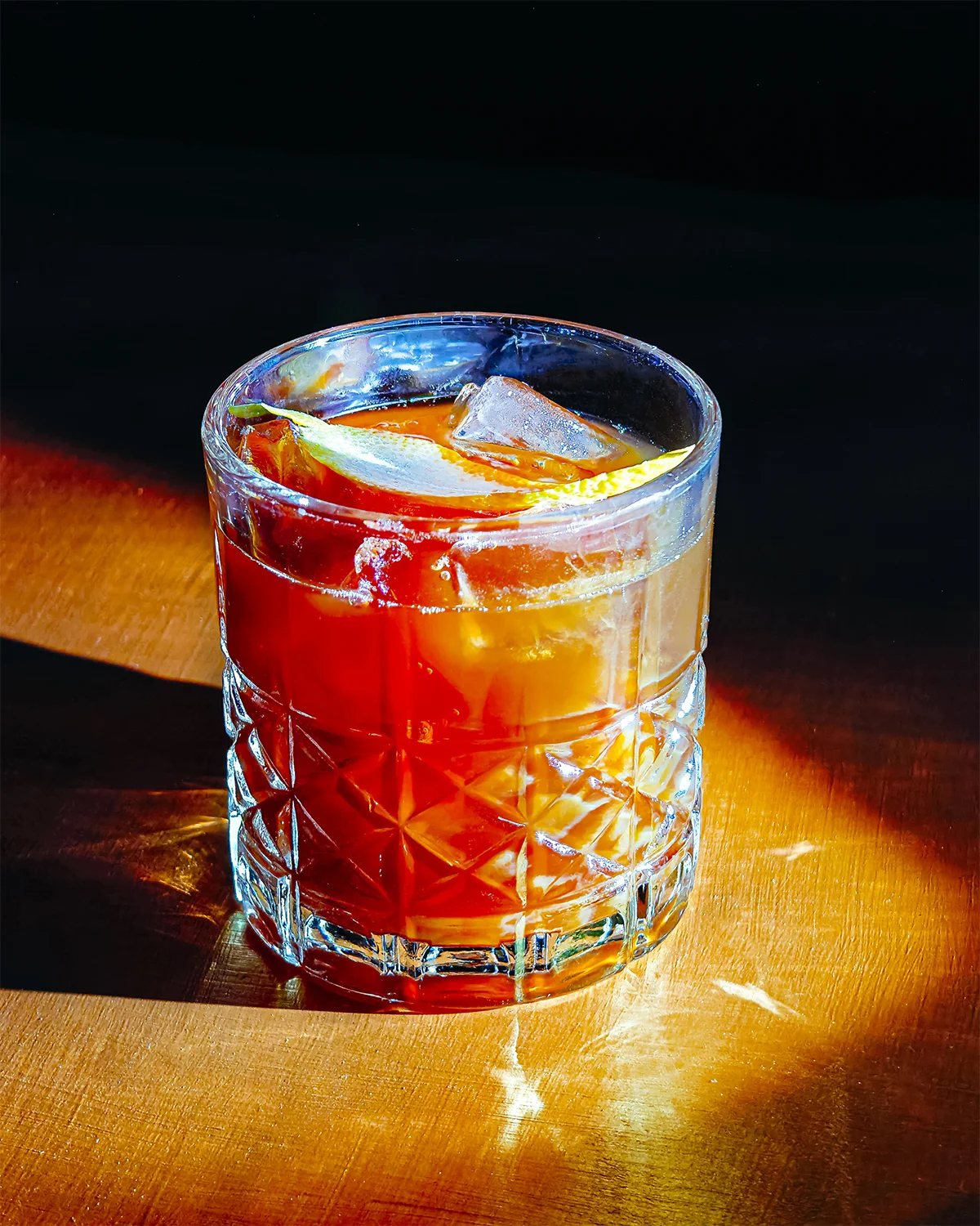 A glass of black tea manhattan with lemon slices on a wooden table.