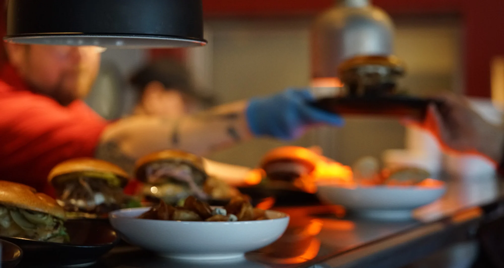 Blurred restaurant kitchen with chefs preparing burgers under pendant lights