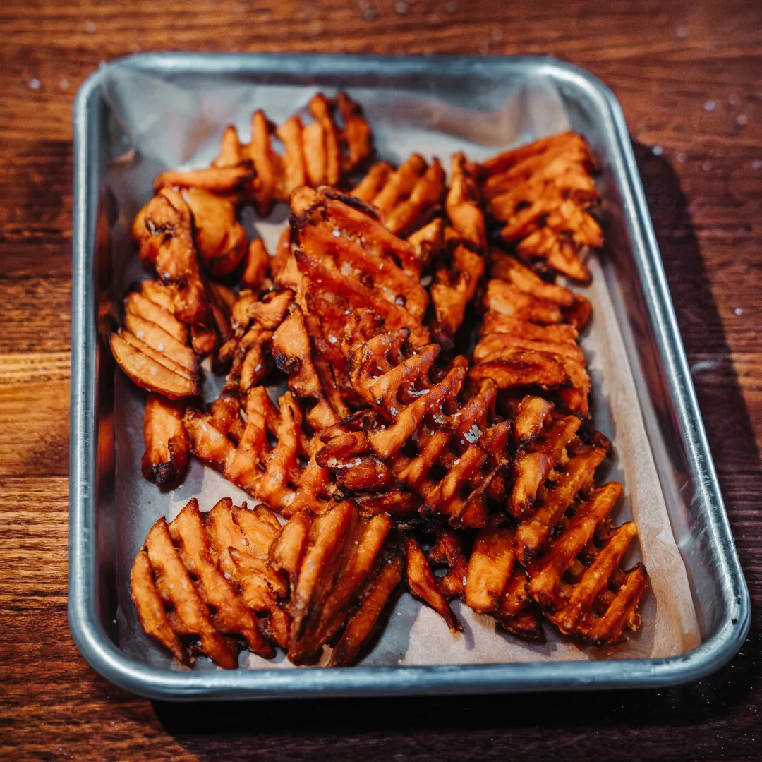 A tray filled with crispy, golden waffle fries, arranged in a casual style.
