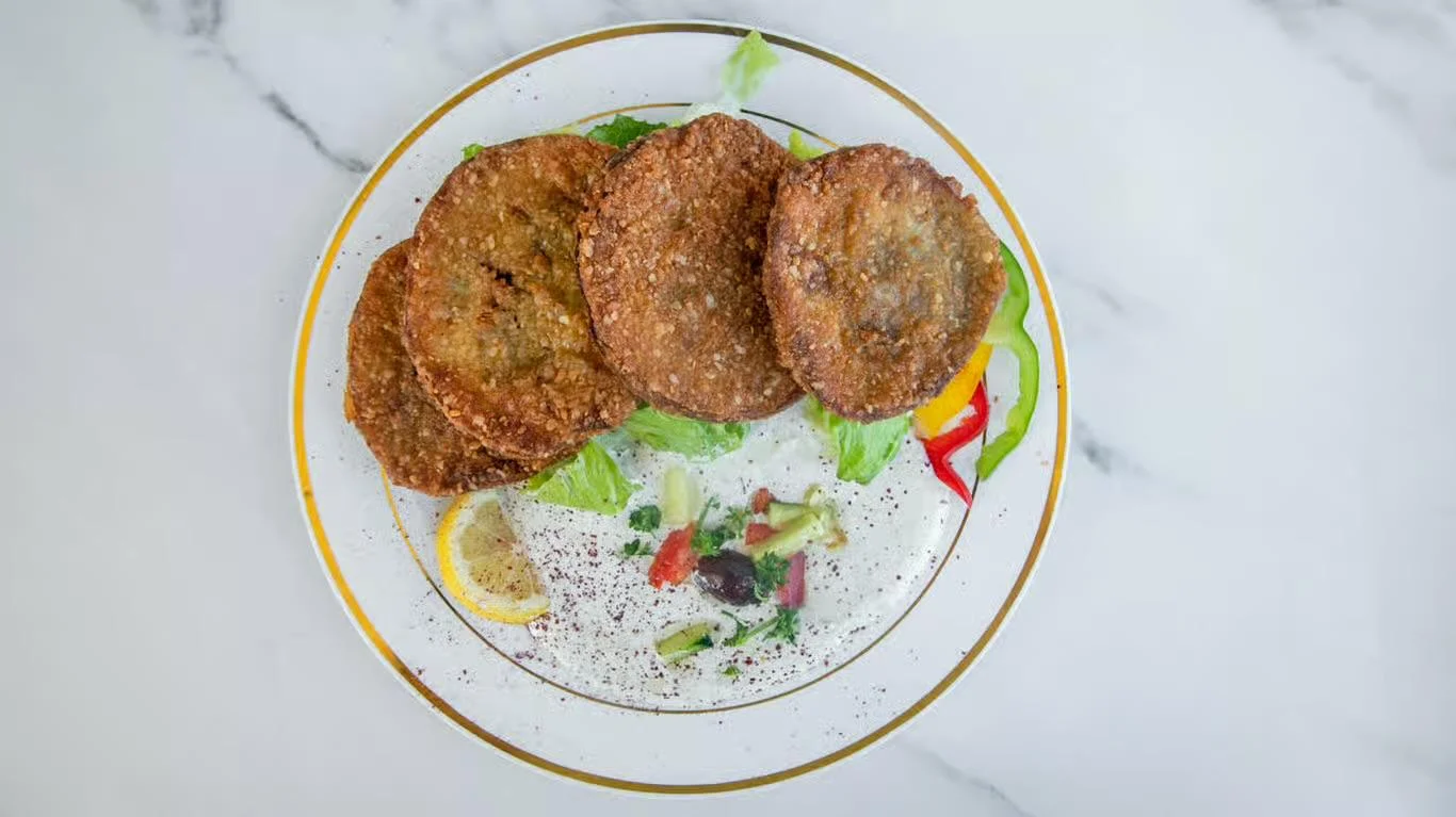 A plate of crispy fried patties arranged on lettuce with a side of fresh salad and lemon slices.