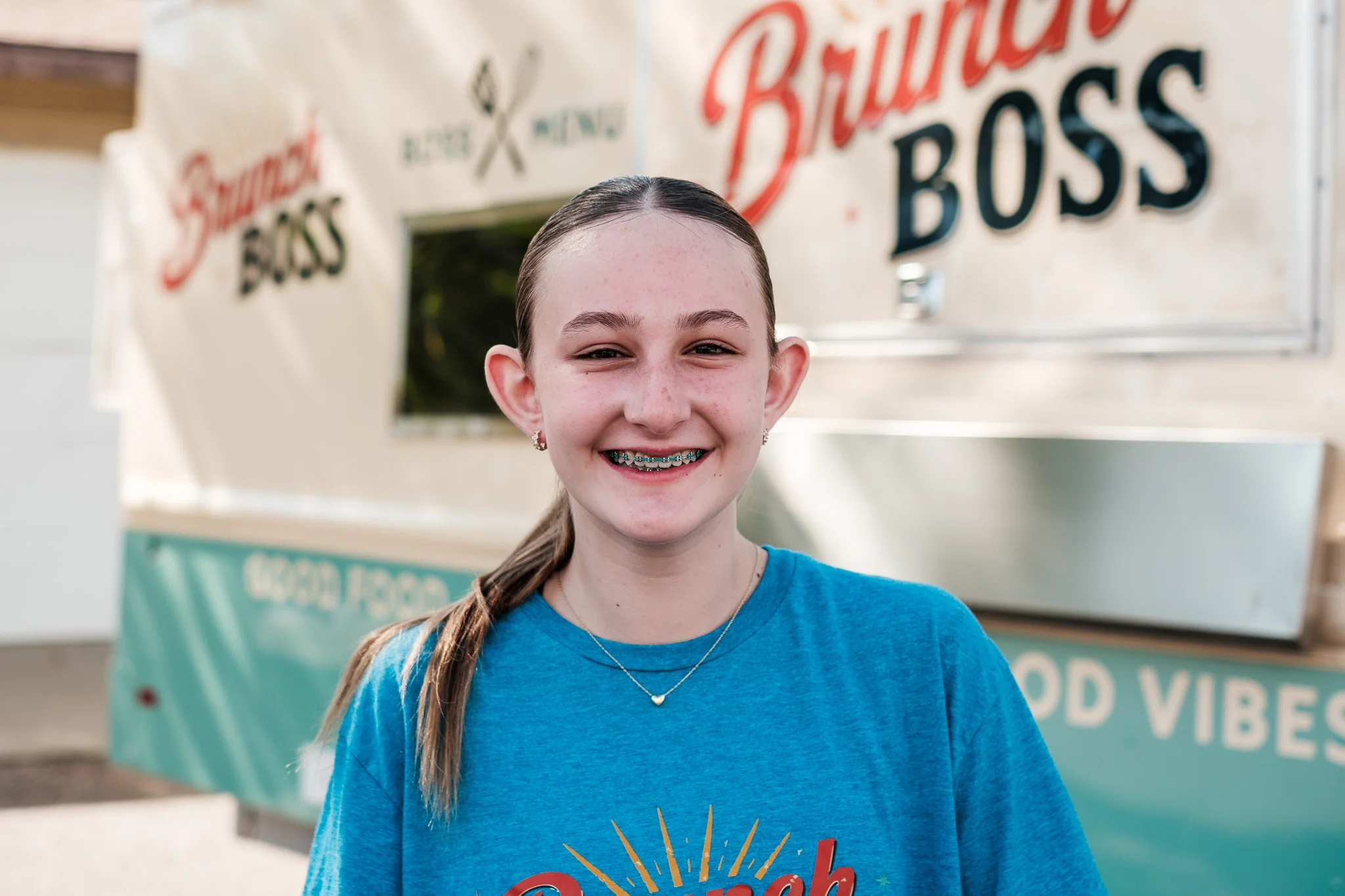 Smiling young girl in a blue Brunch Boss t-shirt by a food truck