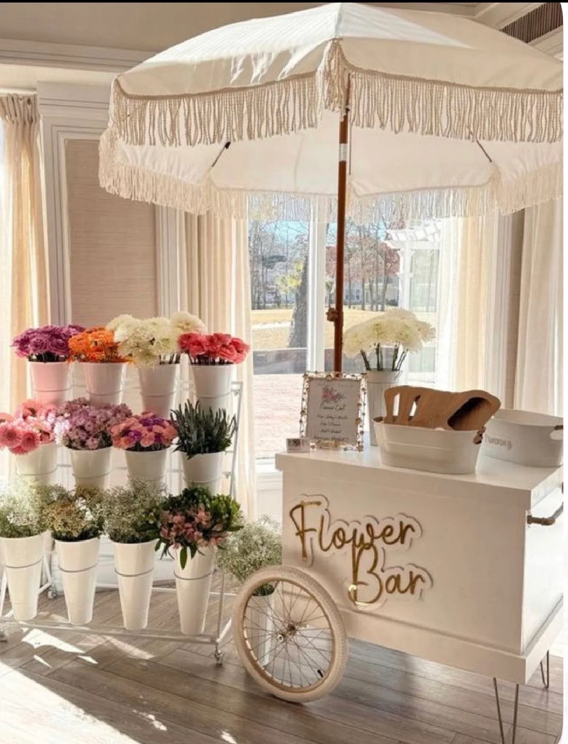 A flower bar setup featuring a white umbrella and vibrant flowers displayed in pots. The bar has a charming, vintage feel.