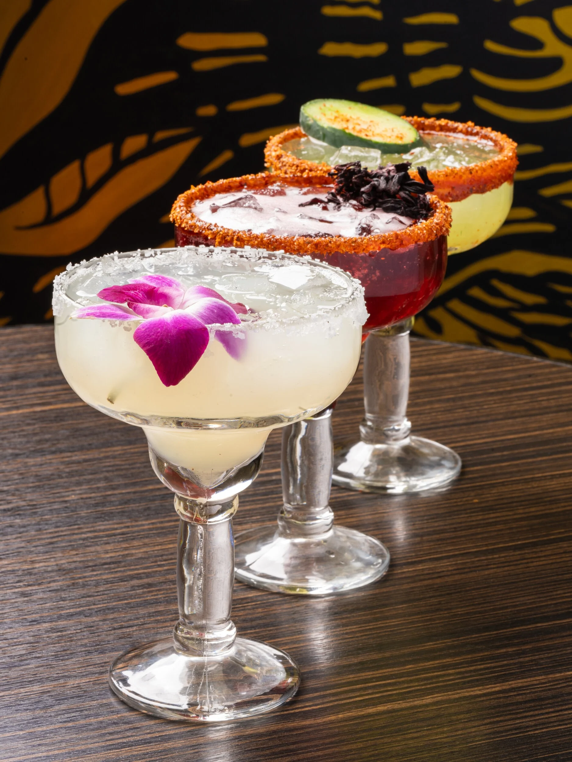 Colorful margaritas with floral garnish at a vibrant bar
