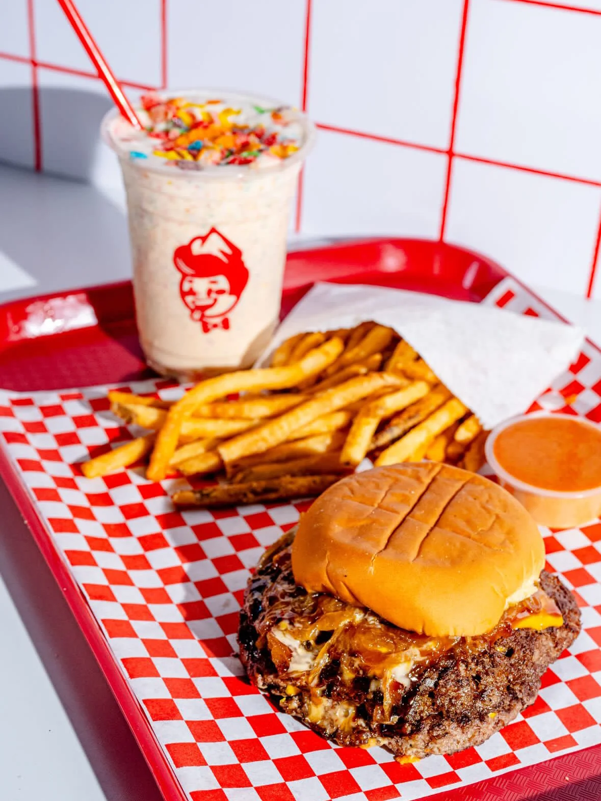 Juicy cheeseburger with fries and a milkshake on a red tray