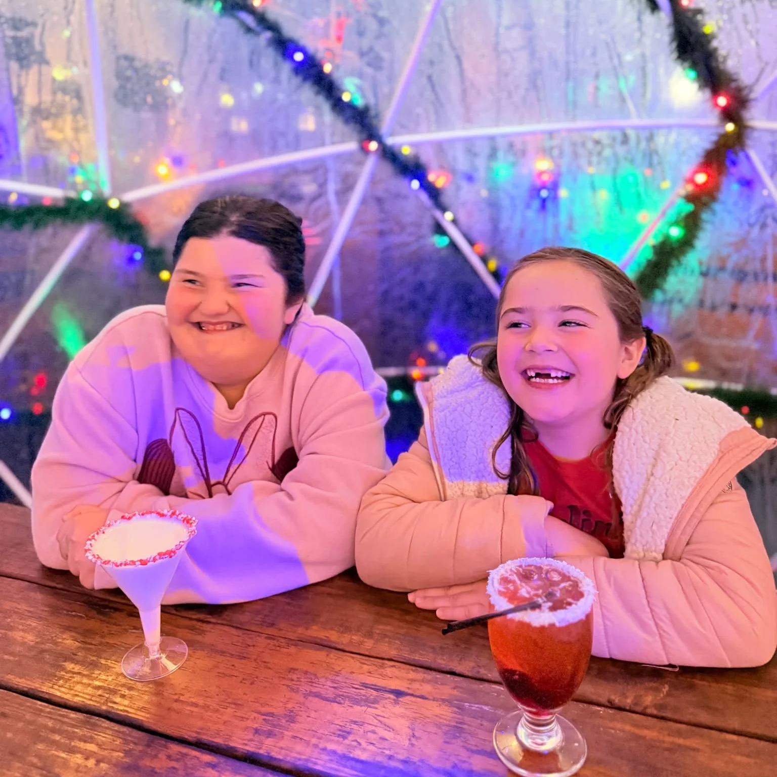 Two people enjoying mocktails inside a cozy igloo setting.