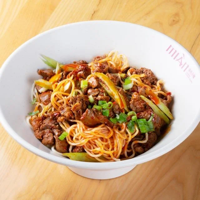 A bowl of chicken gizzard noodle soup garnished with herbs.